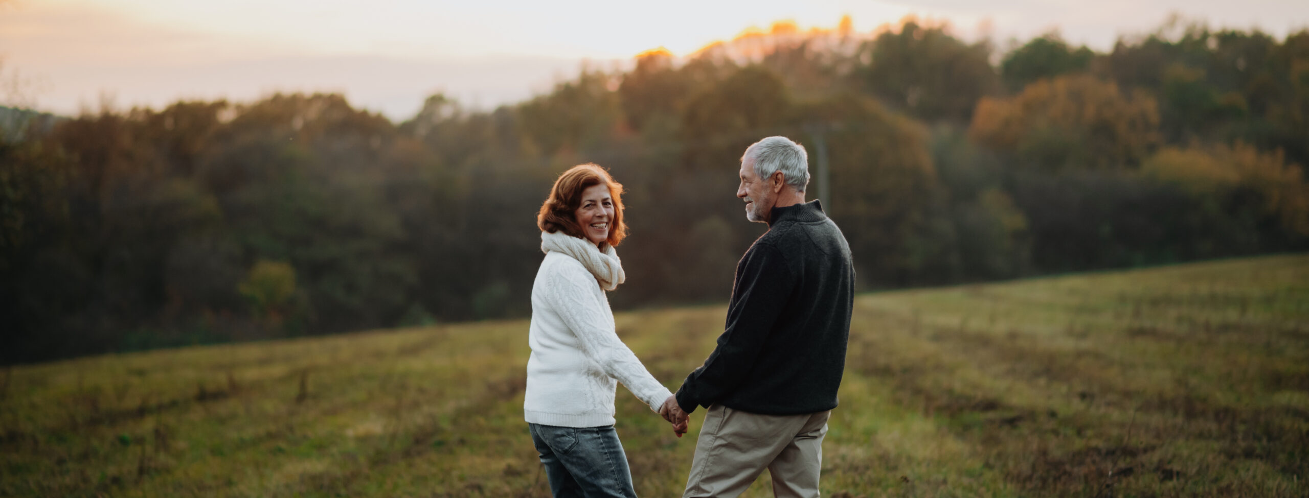 Loving senior couple walking hand by hand in autumn sunset light.