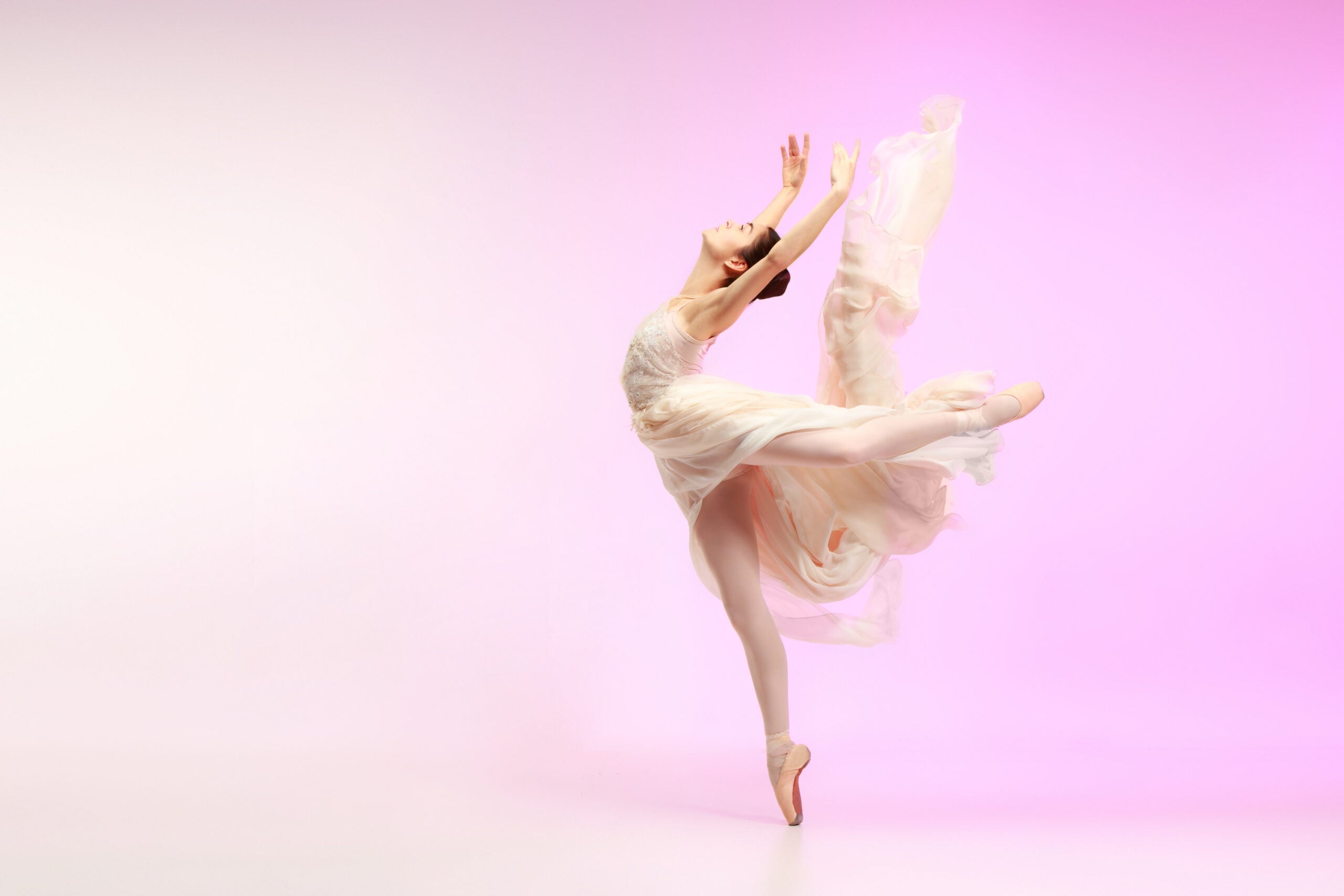 Young graceful female ballet dancer or classic ballerina dancing at pink studio. Caucasian model on pointe shoes
