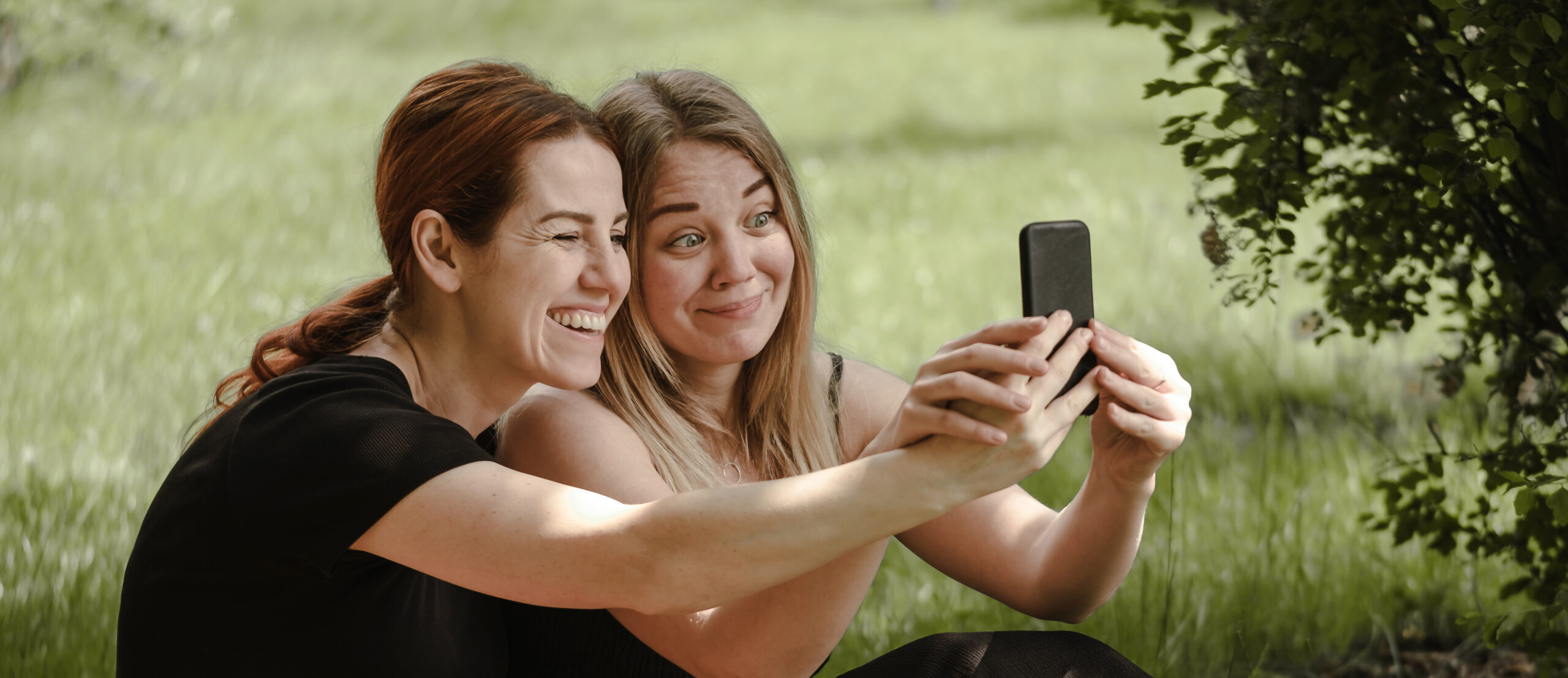 Two woman having fun on picnic. Friends on blanket communicating happily making selfie. Cheerfully female talk outdoors, People laughing and having rest in garden, park with smartphone