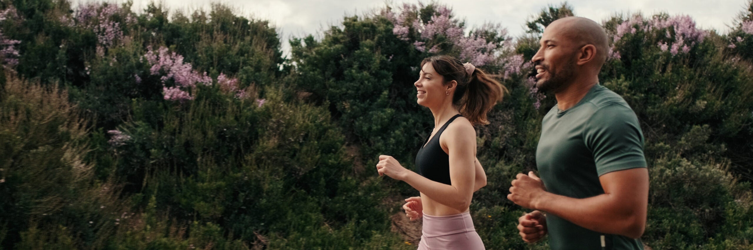Side view of jogging multiethnic woman and man enjoy their outdoors workout in summer. Team sports. Couple goals and motivation. Happy fit people are cheerfully doing sports. For banner. panoramic